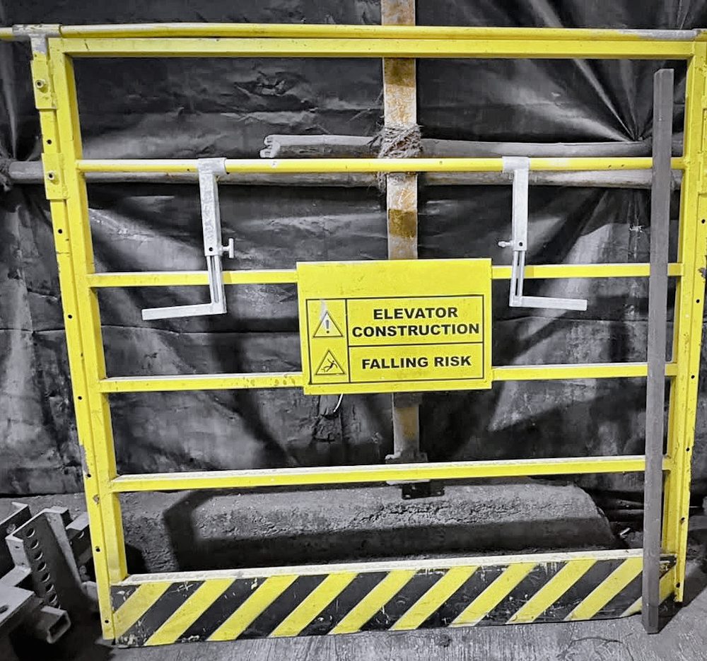 Bar-type barricade with Elevator Construction Falling Risk sign and hazard-striped kick plate